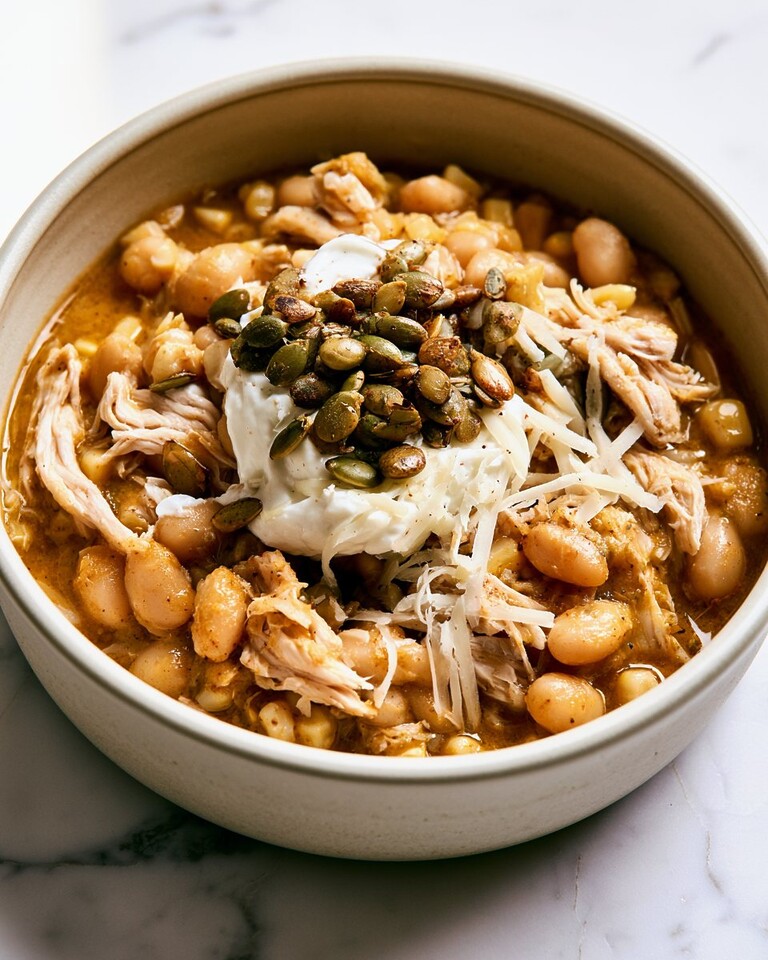 White chicken chili in a ceramic bowl topped with shredded cheese, sour cream, and toasted pumpkin seeds