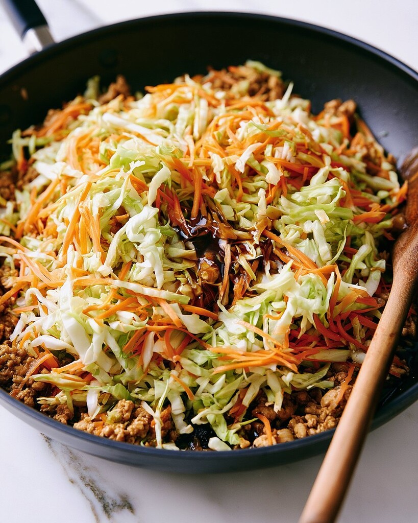 Shredded cabbage and carrots added over browned chicken in a pan