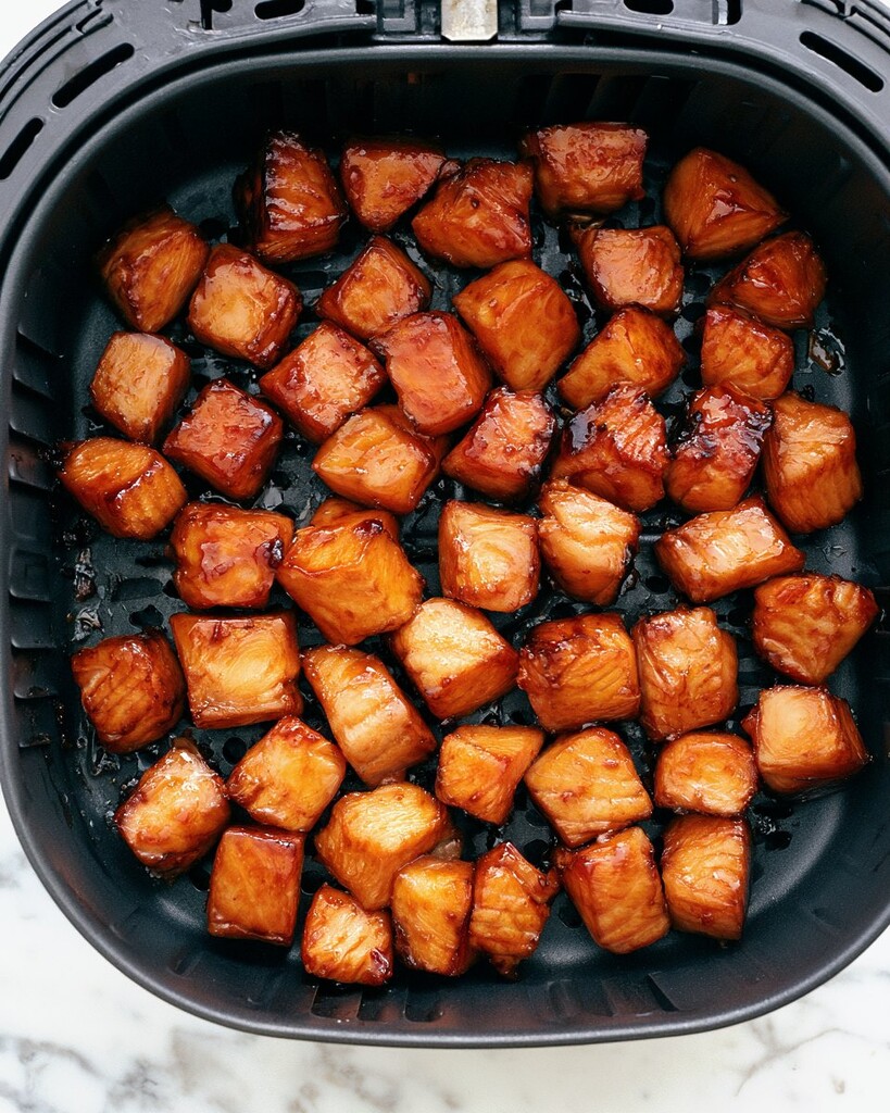 Cubed salmon with caramelized, browned edges resting inside a dark air fryer basket