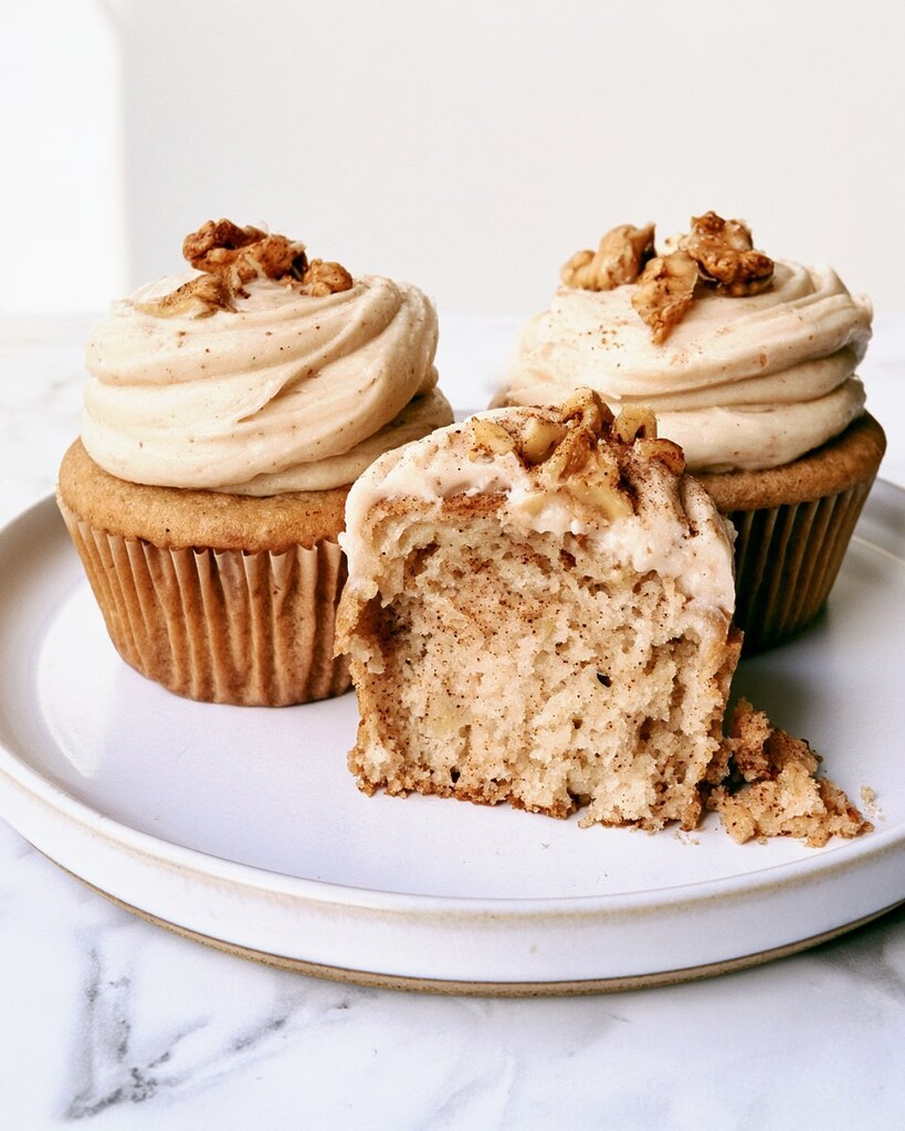 A spiced banana cupcake cut open to reveal the moist internal crumb underneath a thick layer of frosted walnuts