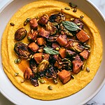 Shallow bowl of creamy orange pumpkin polenta topped with roasted Brussels sprouts, cubed squash, and crispy sage leaves