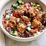 Mediterranean chicken bowl with seared chicken pieces, cucumber, tomato, olives, and crumbled feta over quinoa