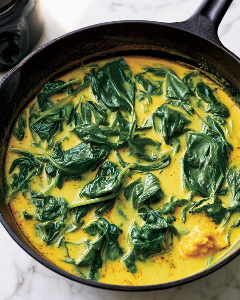 Fresh green spinach wilting into a bright yellow coconut, turmeric, and ginger broth