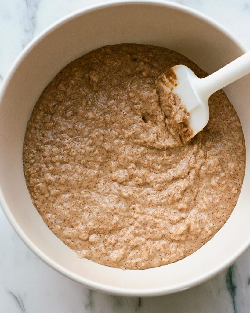 Thick, slightly lumpy whole wheat pancake batter in a white bowl with a silicone spoon