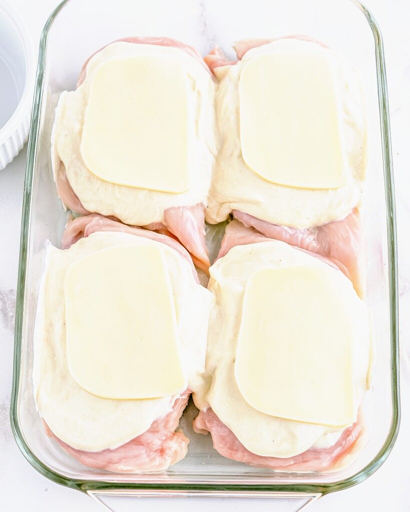 Pounded chicken breasts in a glass dish topped with creamy dressing and provolone slices