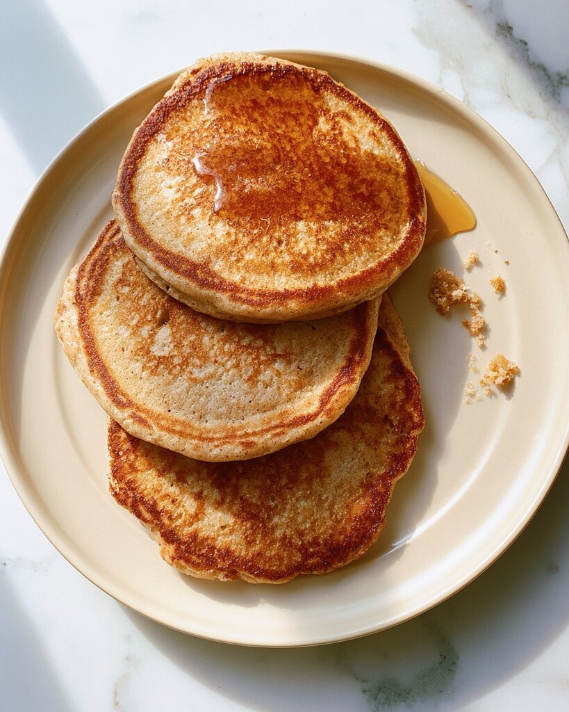 Stack of whole wheat pancakes with browned edges on a light plate, drizzled with syrup