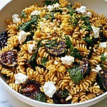 A white bowl filled with blistered zucchini pasta salad, topped with crumbled feta, pine nuts, and green herbs