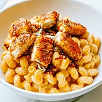 White bowl filled with creamy macaroni and cheese topped with hot honey glazed crispy chicken chunks and bacon
