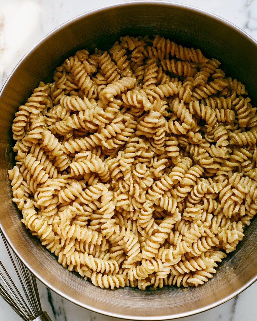 Warm rotini pasta glistening with the freshly mixed pepperoncini vinaigrette inside a large metal bowl