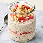 Peanut butter and jelly overnight oats in a glass jar topped with fresh strawberries and roasted peanuts