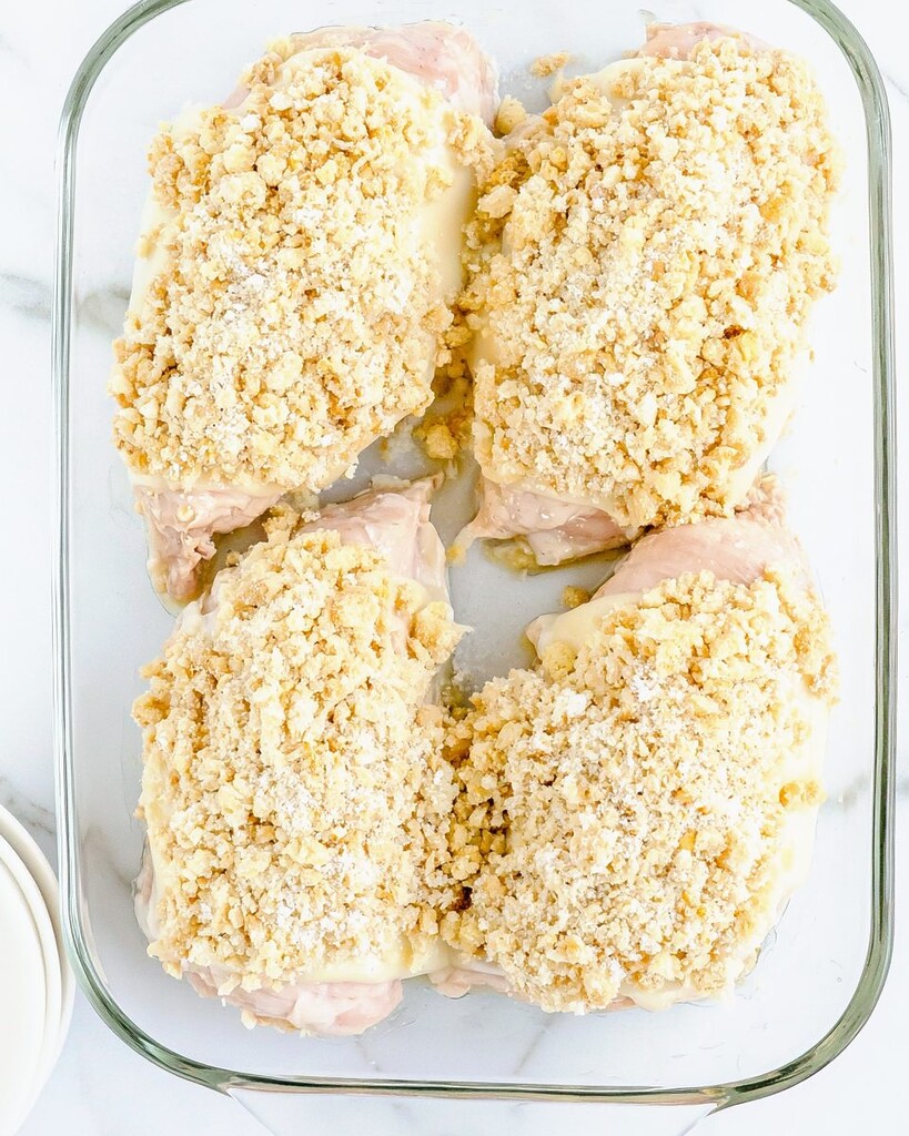 Chicken in a glass dish covered with a pale coarse breadcrumb and crouton mixture