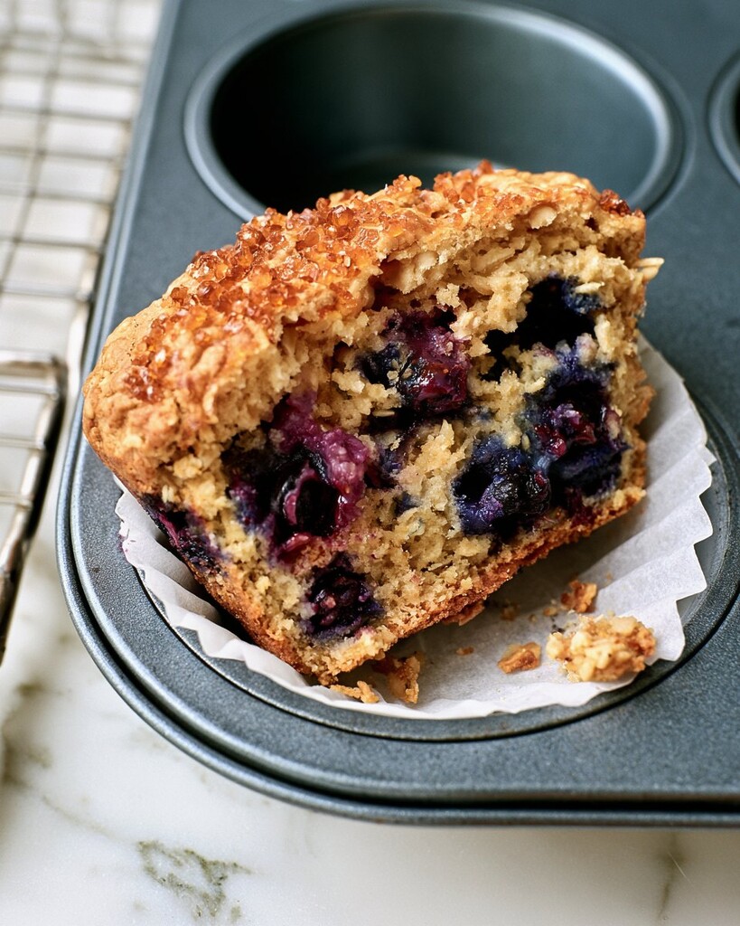 A baked blueberry oatmeal muffin cut in half inside its paper liner showing a moist center and cooked berries