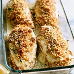 Baked Caesar Chicken with Lemon-Parmesan Crunch Four pieces of baked Caesar chicken in a glass baking dish with a golden brown crust and melted cheese