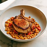 Smoked pork chop in a deep bowl surrounded by soft chickpeas and red peppers