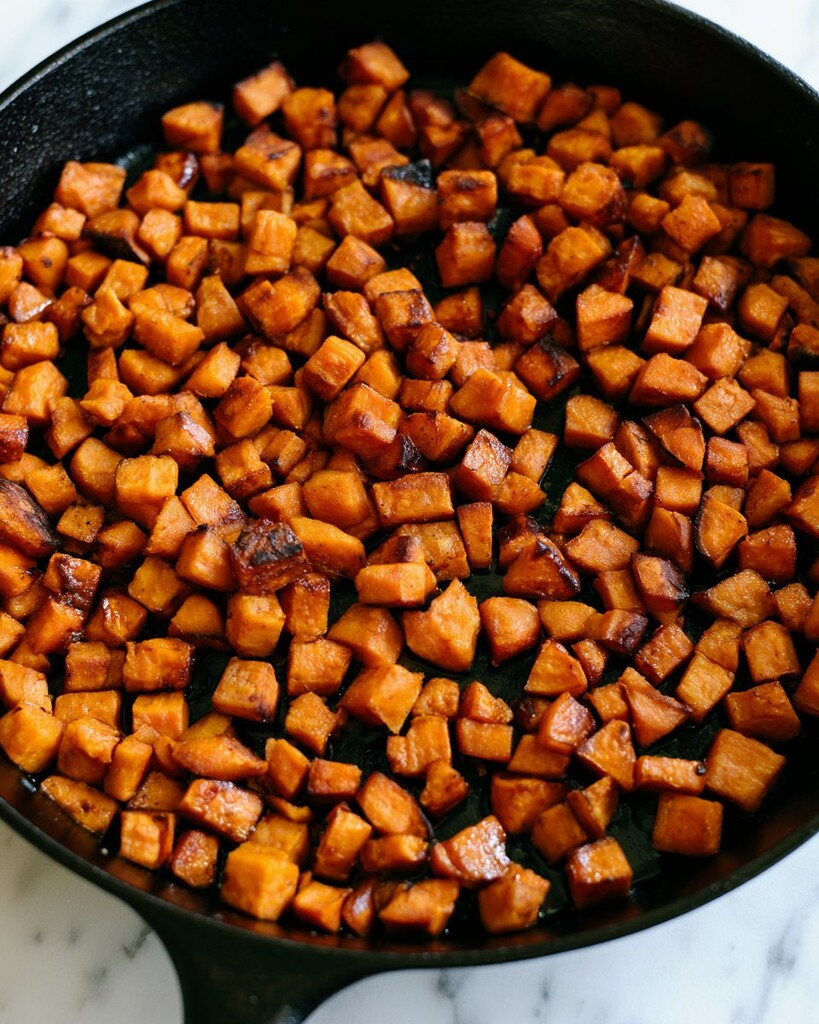Half-inch sweet potato cubes searing in a cast iron skillet with golden browned edges