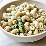 Close-up of creamy cottage cheese macaroni topped with thick swirls of green basil pesto in a ceramic bowl