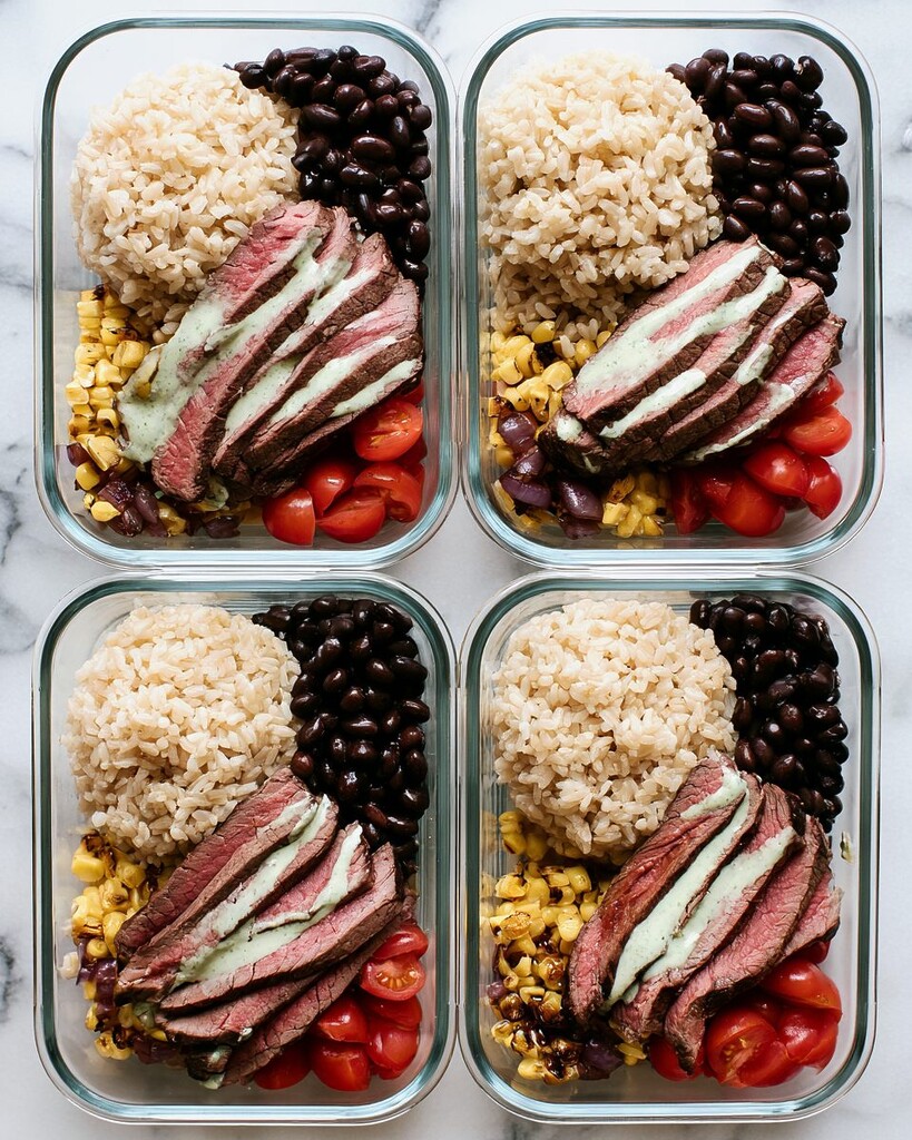 Four glass containers lined up on a counter filled with brown rice, black beans, charred corn, tomatoes, and sliced steak