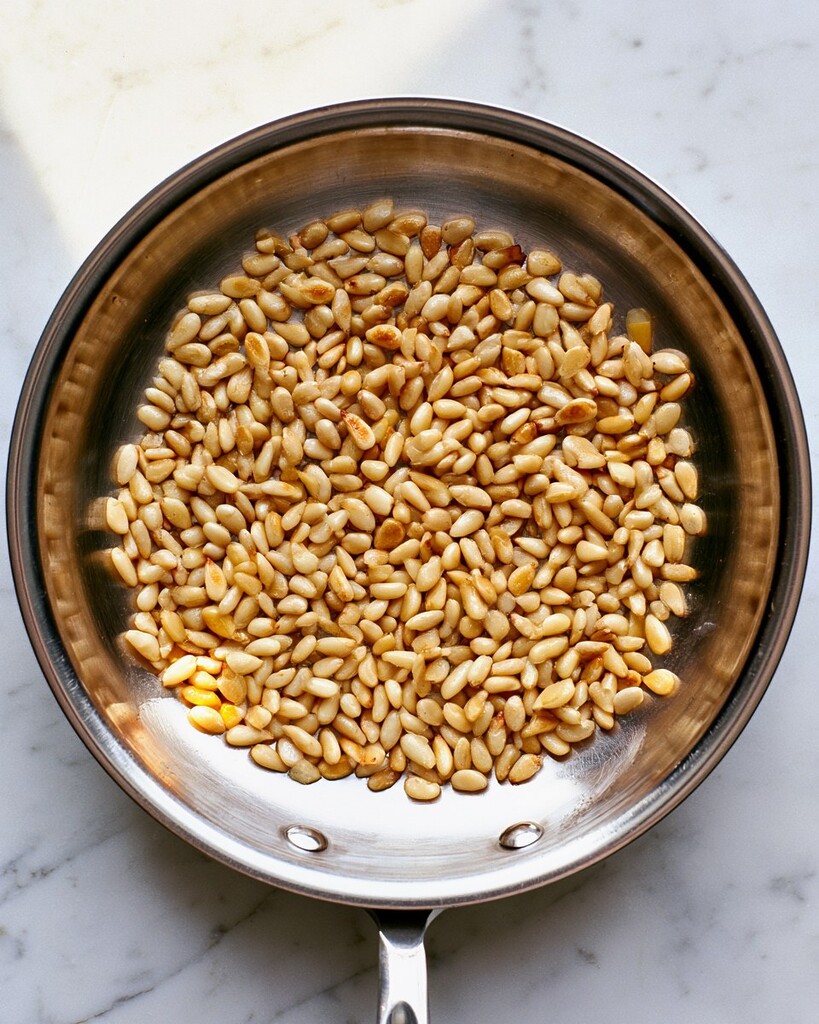 Golden pine nuts toasting in a dry metal skillet over medium heat