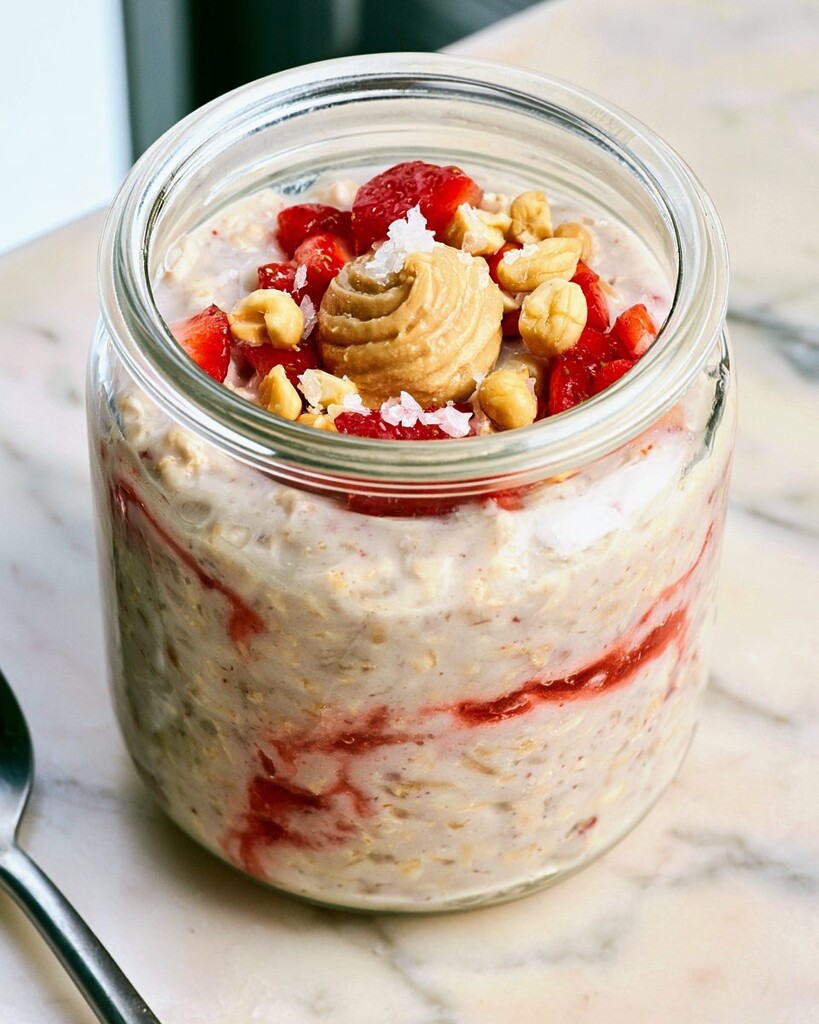 Swirling creamy peanut butter and strawberry jam layers into overnight oats in a glass jar