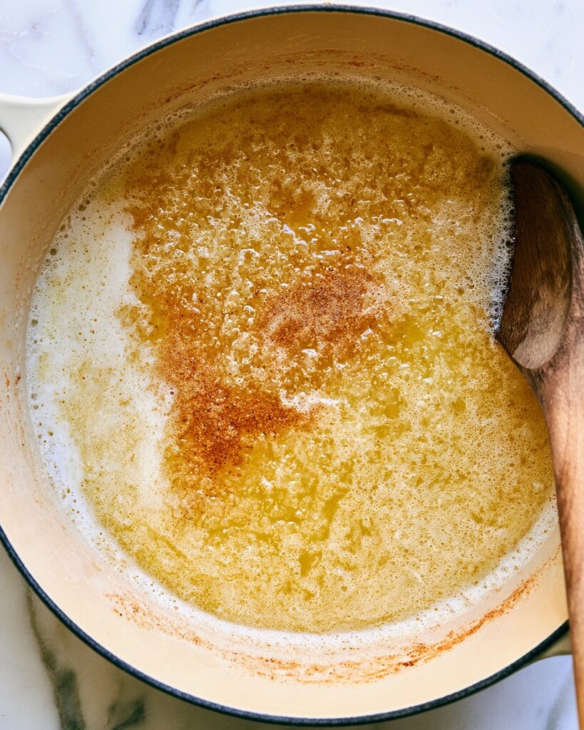 Old Bay butter browning in a light-colored pot with a wooden spoon