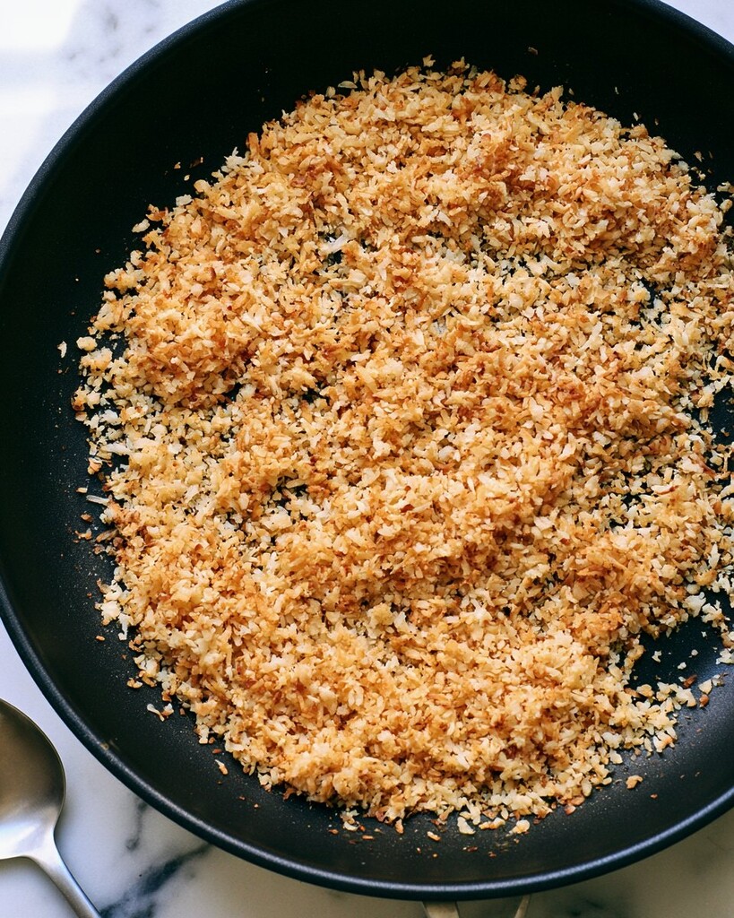 Shredded coconut toasting in a black frying pan until golden brown