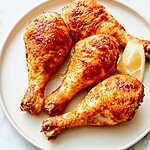 Baked chicken drumsticks with a blistered crust arranged on a platter with lemon slices