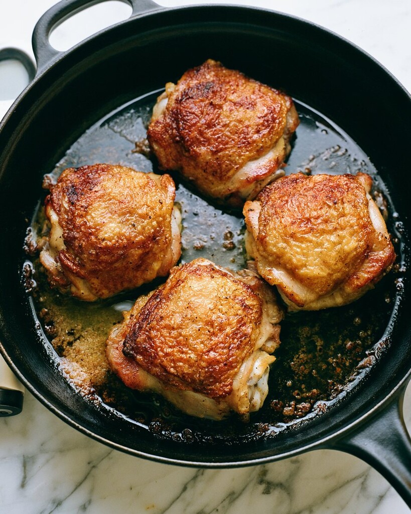 Bone-in chicken thighs searing in a heavy skillet with deep golden, crispy skin