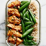 Sheet-pan spicy peanut tofu meal prep bowl with sesame rice, roasted snap peas, and thick brown sauce