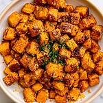 Crispy garlic parmesan roasted sweet potato cubes in a white serving bowl garnished with fresh parsley