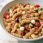 A wide serving dish filled with colorful Italian pasta salad featuring chicken, salami, mozzarella, and crisp vegetables