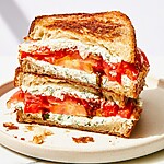 Close-up of a halved tomato sandwich showing thick layers of whipped spread and crispy sourdough edges
