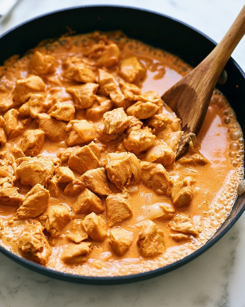 Creamy coconut chicken pieces returning to the orange sauce in the skillet