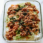 Chicken egg roll bowl served over rice in a glass container with sriracha mayo, sesame seeds, and scallions