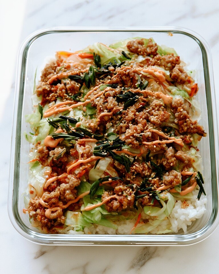 Chicken egg roll bowl served over rice in a glass container with sriracha mayo, sesame seeds, and scallions