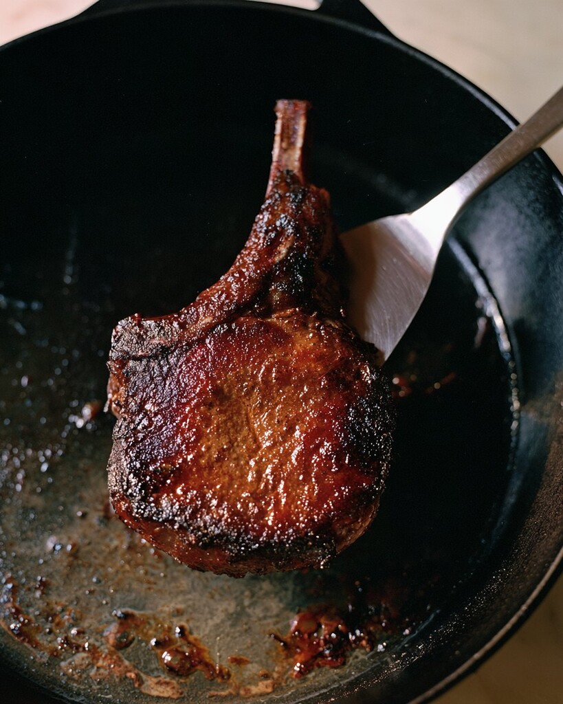 Lifting a dark seared pork chop from a cast iron pan with a metal spatula
