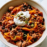Thick turkey chili mixed with orange butternut squash noodles and black beans, topped with sour cream, pumpkin seeds, and green onions.