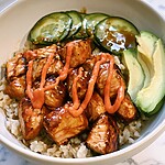 Brown rice bowl topped with glossy salmon chunks and lines of spicy mayonnaise