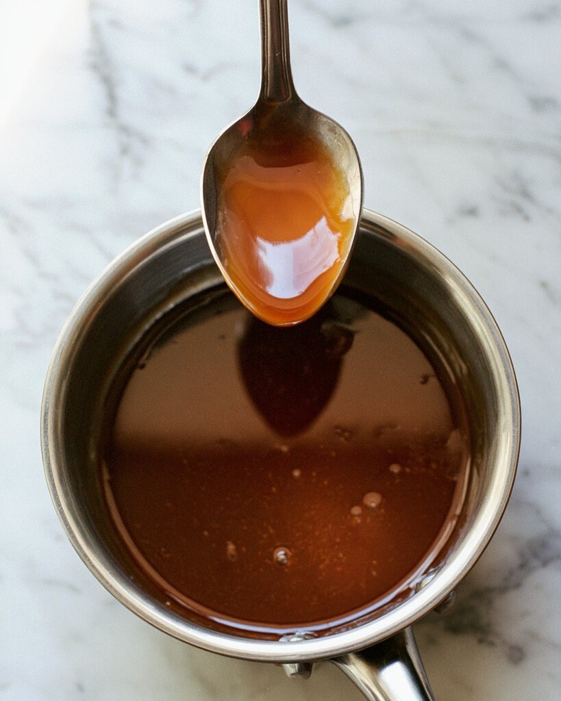 A spoon lifting dark, thickened teriyaki sauce out of a small saucepan