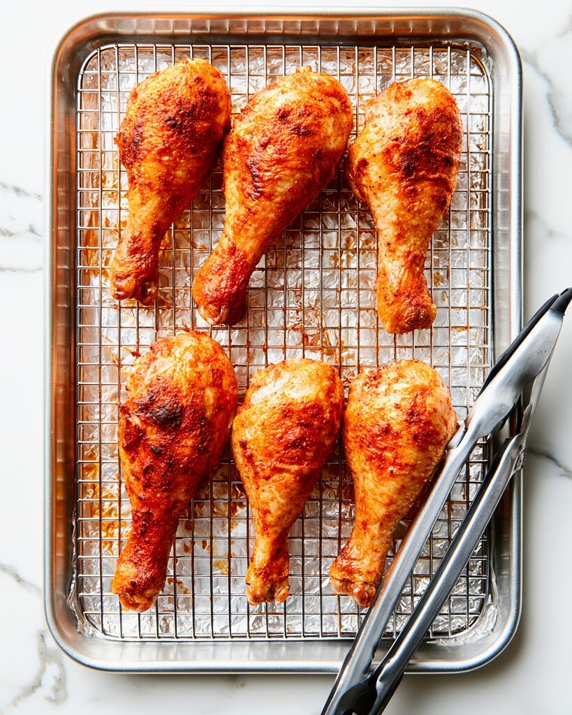 Freshly baked chicken drumsticks with blistered golden skin resting on a wire cooling rack