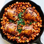 One-Pan 30-Minute Honey-Chipotle Chicken and Sweet Potatoes Cast iron skillet filled with glazed honey-chipotle chicken thighs and roasted sweet potatoes, garnished with fresh cilantro and lime wedges