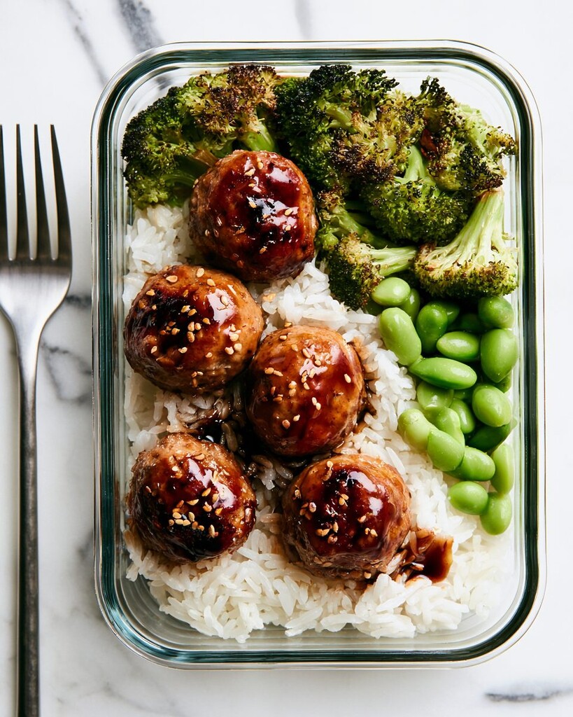 Meal prep container filled with white rice, roasted broccoli, cooked edamame, and glazed meatballs