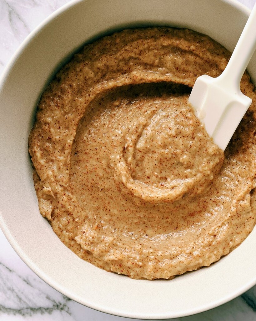 Thick cupcake batter speckled with brown spots sitting in a light colored bowl with a silicone spatula