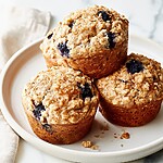 Three finished blueberry oatmeal muffins stacked on a plate highlighting the baked texture