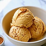 Three creamy scoops of pumpkin ice cream with Biscoff cookie crumbs in a light ceramic bowl