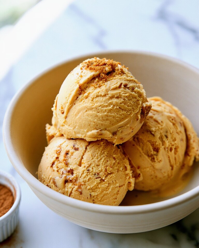 Three creamy scoops of pumpkin ice cream with Biscoff cookie crumbs in a light ceramic bowl