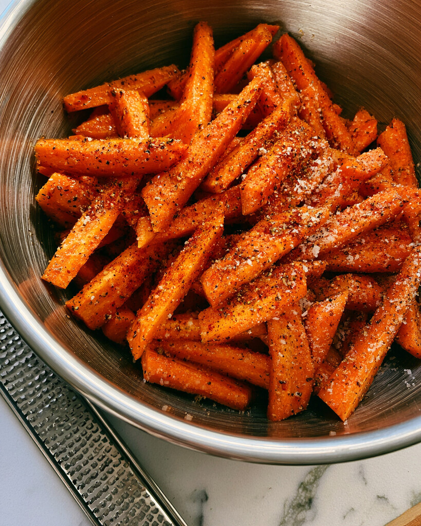 Chopped carrots tossed with olive oil, fine Parmesan cheese, and spices in a metal mixing bowl