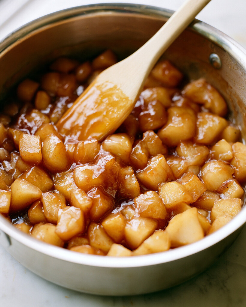 Diced spiced pears cooking in a metal saucepan surrounded by a glossy amber liquid