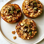 Golden pumpkin baked oatmeal cups on a light plate topped with shiny pumpkin seeds