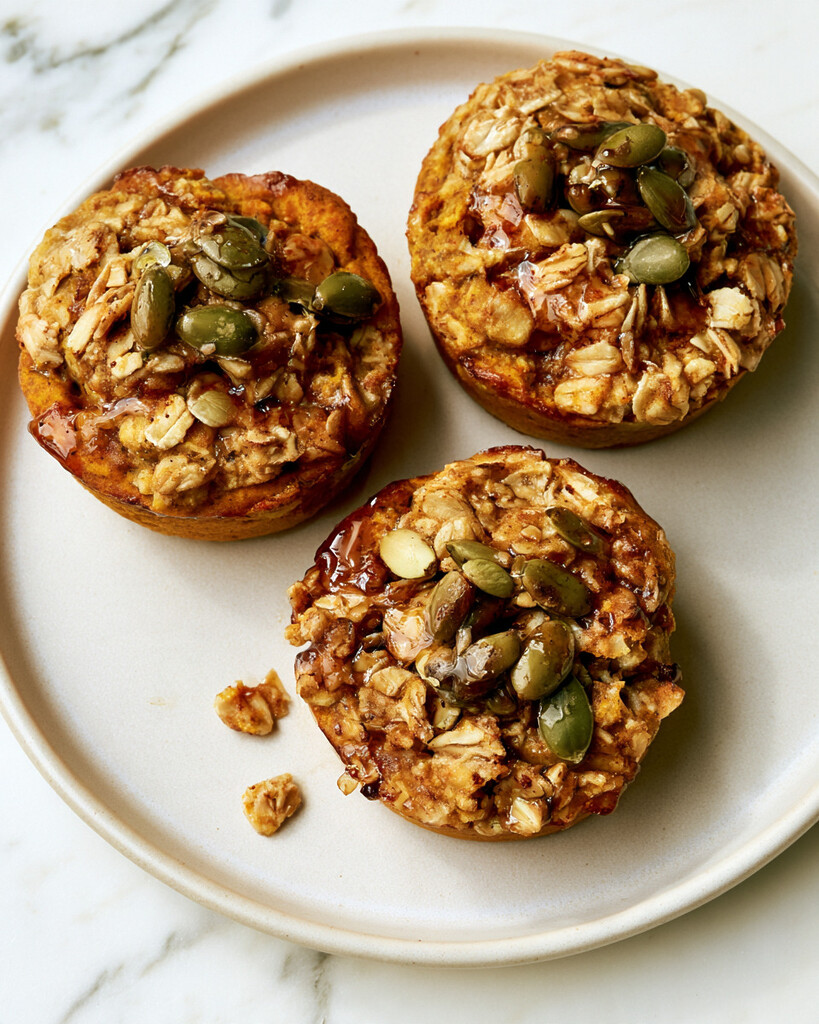 Golden pumpkin baked oatmeal cups on a light plate topped with shiny pumpkin seeds