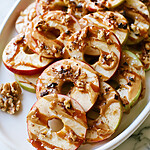 Date caramel apple ring nachos topped with walnuts and chocolate on a white plate